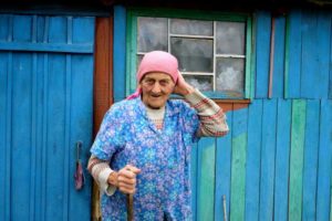 starsza kobieta w chustce przed drewnianym domem