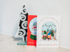 pocztówki świąteczne oparte o szklaną choinkę na białym tle