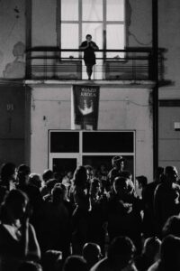 fotografia czarno biała: mężczyzna stoi na balkonie, pod nim tłum ludzi